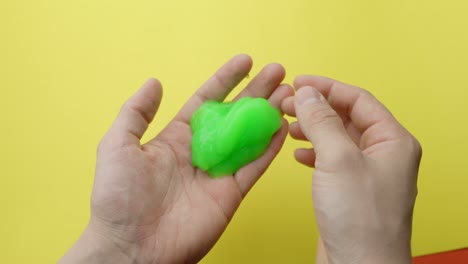 hands stretching and pressing a wavy green slime toy for asmr and stress relief against a yellow background, highlighting texture and movement, static camera, real time, close-up view