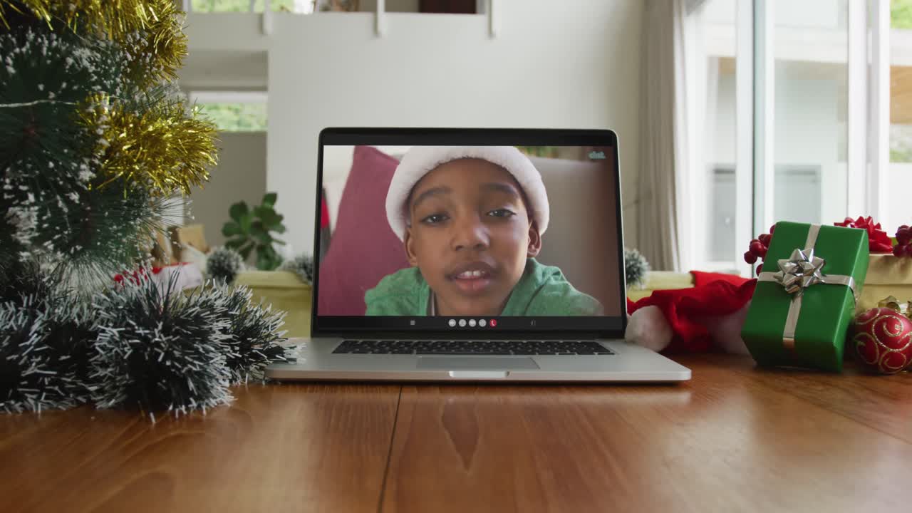 un niño afroamericano sonriente con sombrero de santa en una videollamada de navidad en una computadora portátil