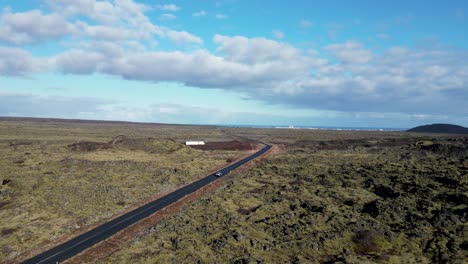 A-car-winding-through-Icelandic-highlands,-mossy-terrain,-hills,-and-vast-plain