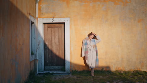 relaxed woman leaning rustic building with textured doorway at sunset sunlight.