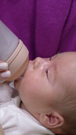 sweet little baby eating milk from a bottle in mommy's hands. baby finishing the bottle and lets go the bottle pacifier. suckling baby close up. vertical video