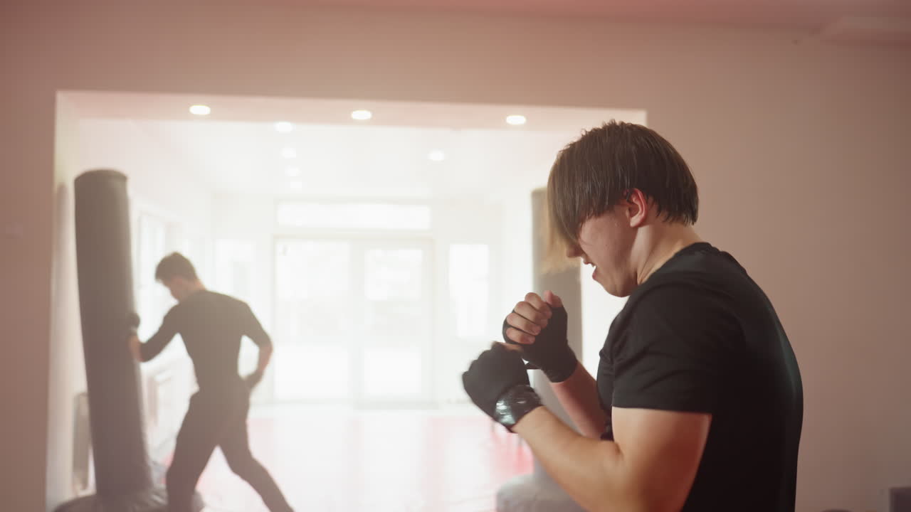 Athlete in black sportswear trains with intensity inside gym, throwing fast punches while sparring partner practices in background, showcasing power, movement, discipline, and energy during combat workout