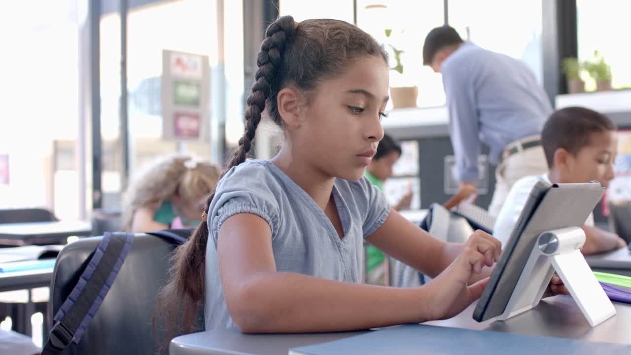 Una ragazza birazziale concentrata sul suo tablet a scuola in classe.