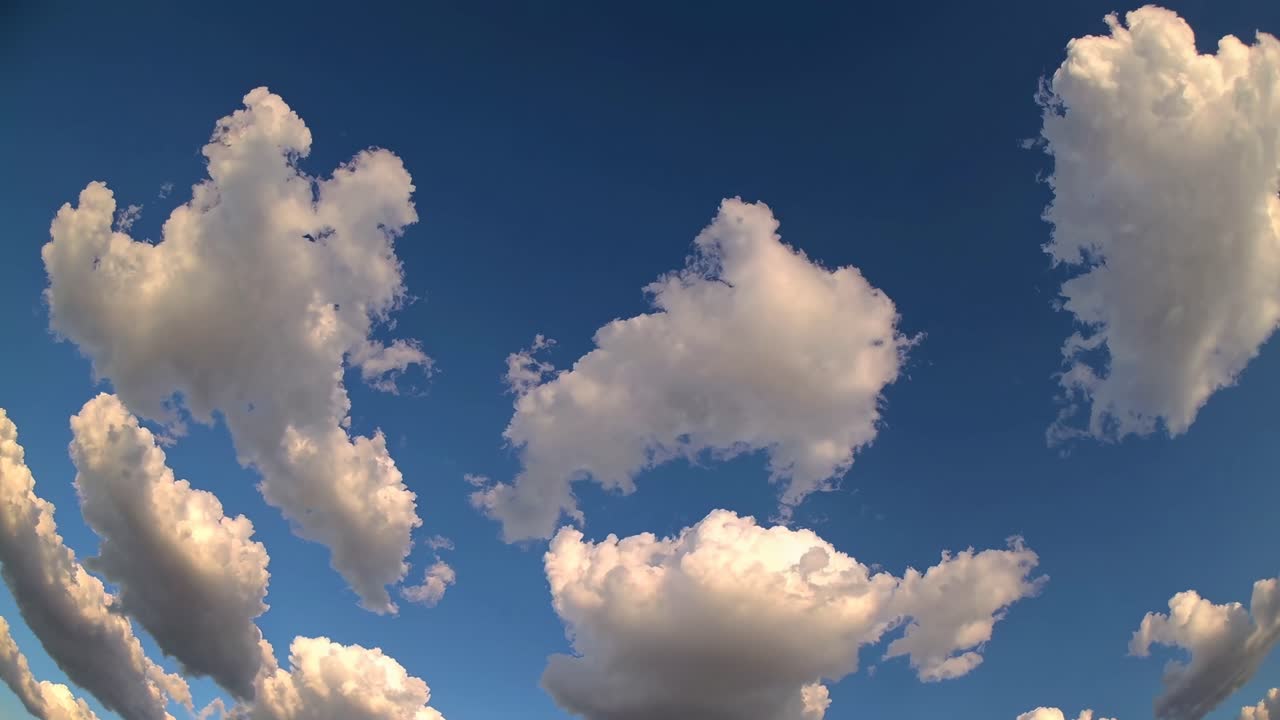 A fisheye lens captures fluffy clouds against a vivid blue sky, creating a surreal, expansive view