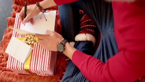 biracial man writing christmas greetings on christmas card at home, slow motion