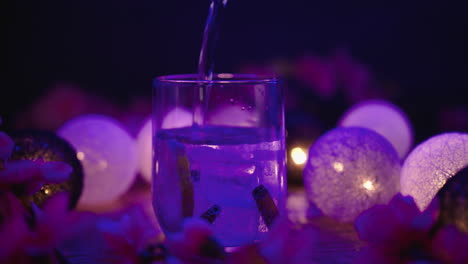 slow motion product video of a lowball glass being filled with a tonic drink with ice blocks and vanilla sticks, surrounded by atmospheric lights