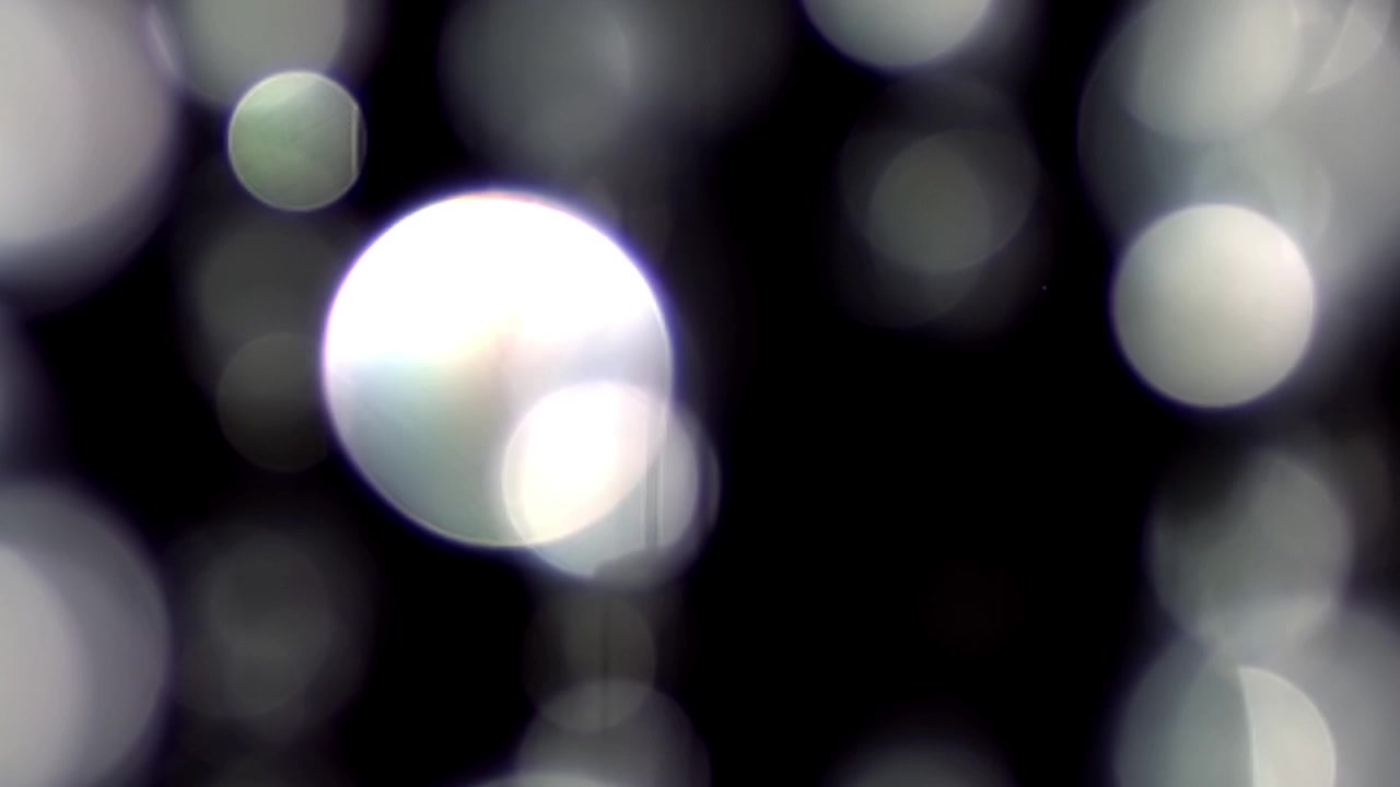 Eteriska vita bokeh-ljus som svävar på svart bakgrund