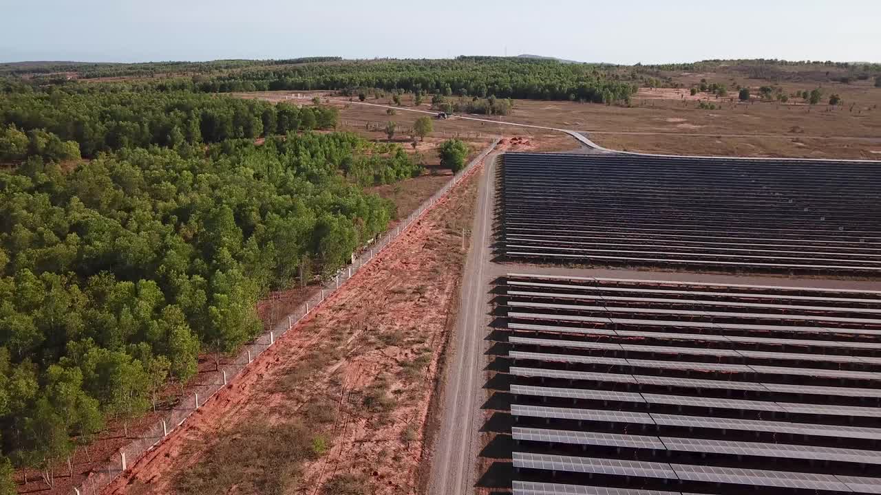 fence and road for securing a solar power plant in Vietnam. red sand and trees separated by the fence