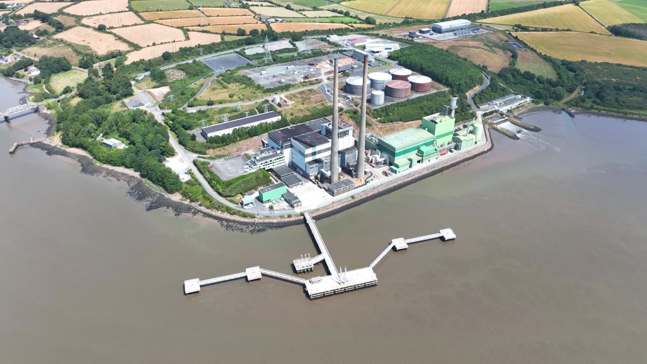 drone pullback capturing renewable energy power station on the River Suir, Wexford, Ireland. Detailed aerial views of electricity infrastructure with vibrant rural scenery.
