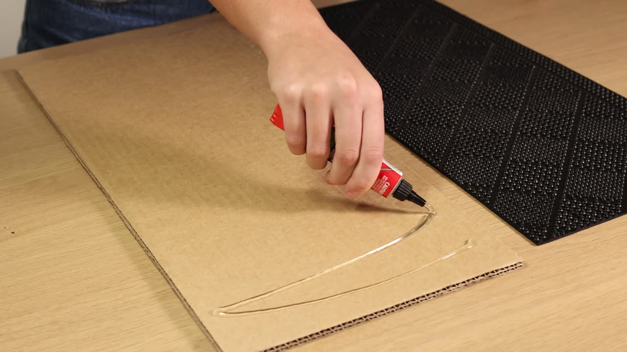 A person applies glue to a cardboard sheet in a well-lit workspace, preparing for a surface experiment