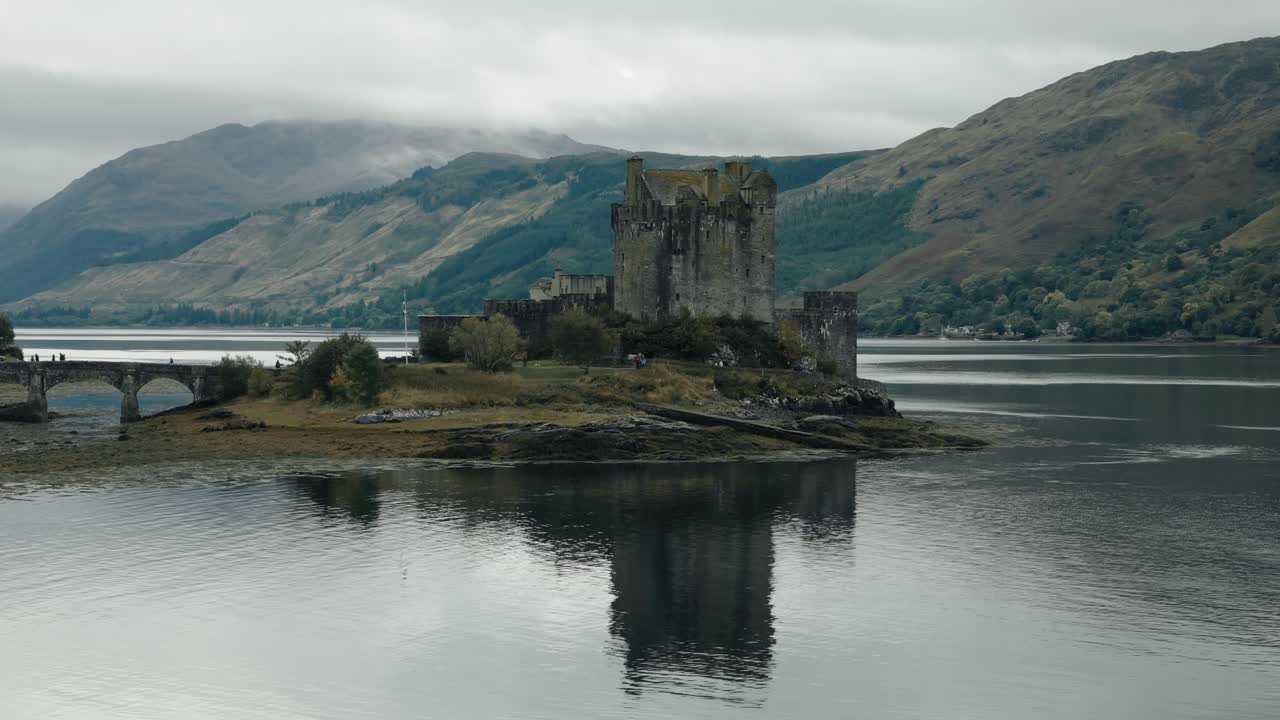 Aerial low orbit view of Eilean Donan Castle in the Scottish Highlands, Scotland, set against a picturesque loch and rugged highland scenery