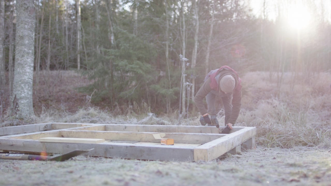 Händig kvinna använder borrmaskin för att fästa undergolvet i golvbjälkarna vid bygget av ett minihus.