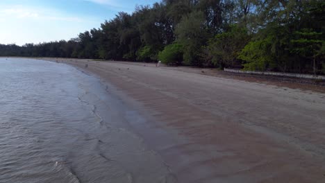 Krabi-Ao-Nang,-Sea-washing-a-tropical-beach-with-tourists-walking-on-the-sand-and-green-hills-in-the-background