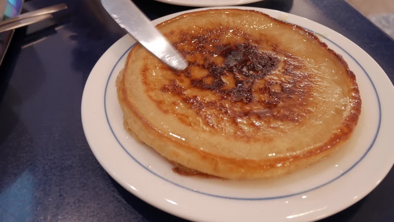 Fluffy pancake being cut, dripping with butter and syrup on a white plate