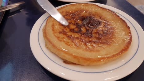 fluffy pancake being cut, dripping with butter and syrup on a white plate
