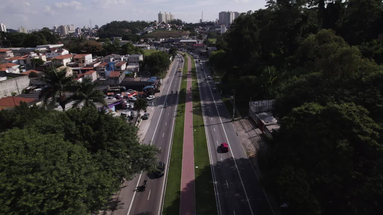el dron avanza recto por una avenida con un carril bici en el medio, algunos árboles a un lado y edificios de la ciudad de são paulo al otro lado