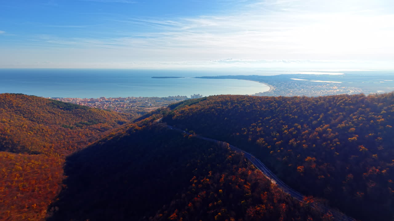 Vista aerea distante di una strada di montagna che serpeggia tra le colline verso una città costiera e una baia marina all'orizzonte