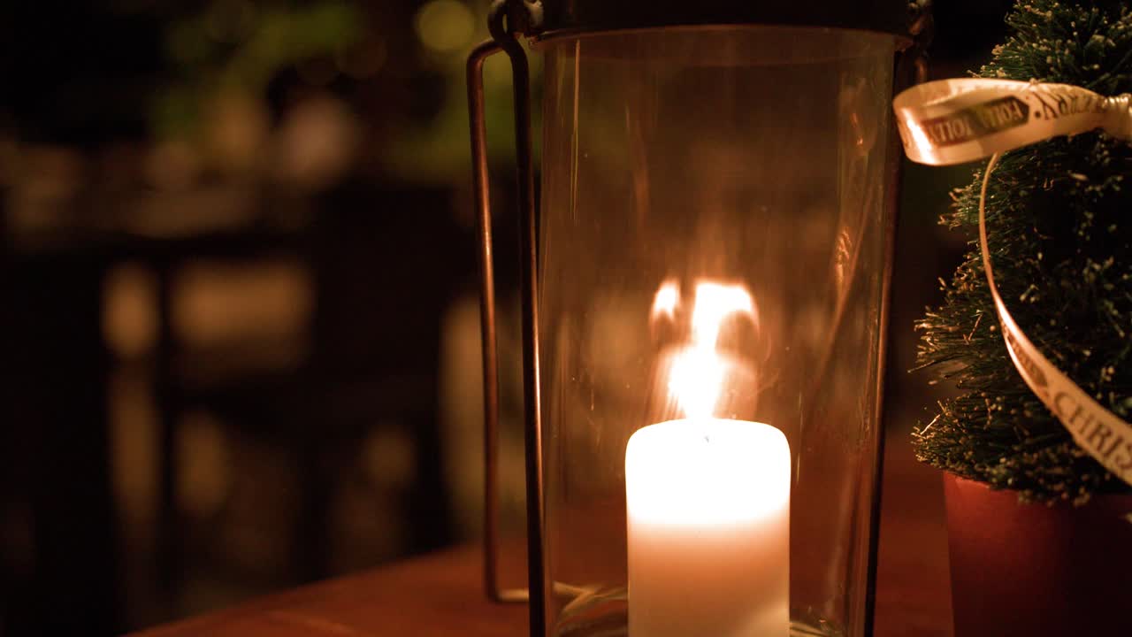Primo piano di una fiamma di candela accesa all'interno di un cilindro di vetro con sfondo bokeh caldo