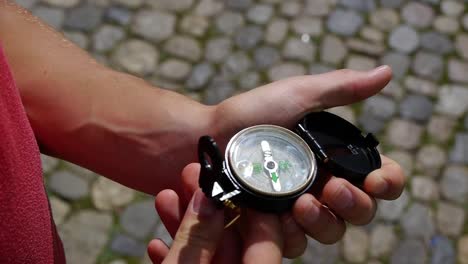 young man takes out a compass and opens it, the sun is reflected in it