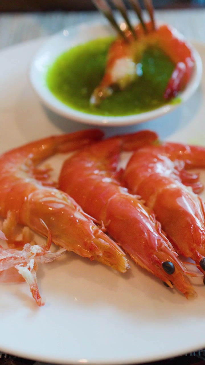Una forchetta prende un gambero cotto e lo intinge in una salsa verde piccante.