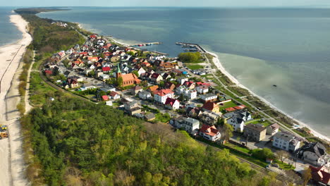 Aerial-view-of-Kuźnica,-a-coastal-village-on-the-Hel-Peninsula,-Poland,-showcasing-its-vibrant-residential-area,-sandy-beaches,-and-the-surrounding-green-landscape