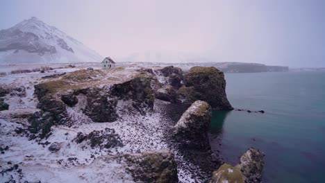 a house is seen overlooking arnarstapi harbor on the snaefellsne peninsula of iceland with snow on the ground 1