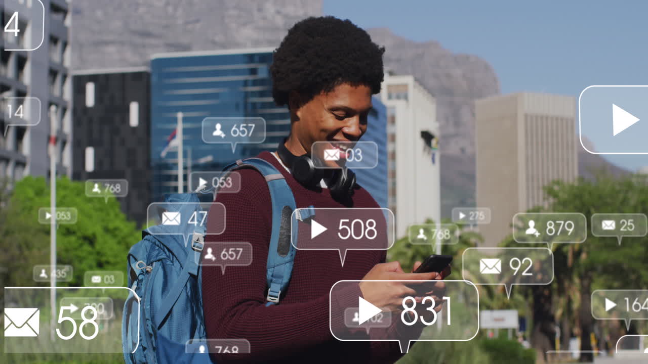 Animation of social media icons over happy african american man using smartphone on the street