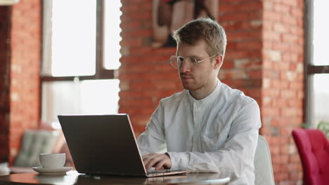 attractive young man is working with laptop in cafe freelancer and independent journalist typing text on keyboard