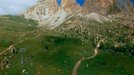 A-group-of-tiny-mountain-bikers-roll-across-green-pastures-in-front-of-the-dramatic-rock-face-of-the-Langkofel---Sassolungo-massif