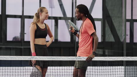 smiling diverse athletes discussing padel tennis strategy on court, holding rackets