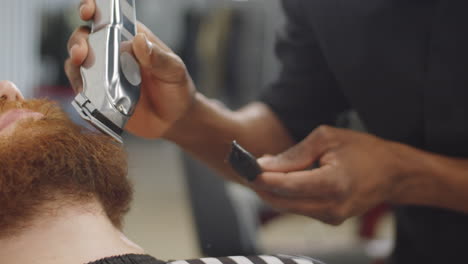 black barber trimming of beard of man with clippers