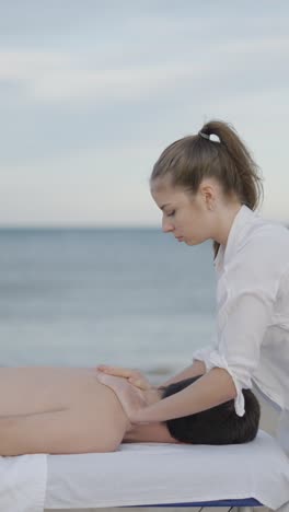 woman gives relaxing back massage to man on beach