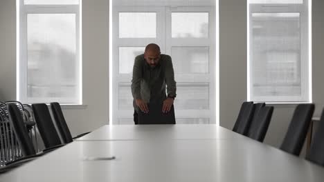 nervous bald indian manager alone in empty meeting room waiting for colleagues, tapping fingers on empty chair