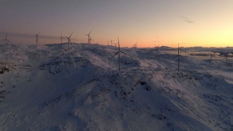 wind turbines atop snow-covered mountain at sunset in arctic circle