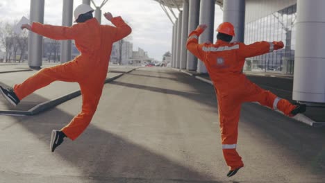 two happy construction workers in orange uniform and helmets walking and jumping together