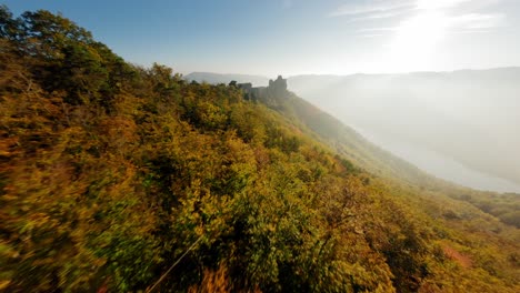 FPV-approaching-beautiful-Aggstein,-passing-a-stone-formation-on-green-wachauer-hills-in-autmn-light