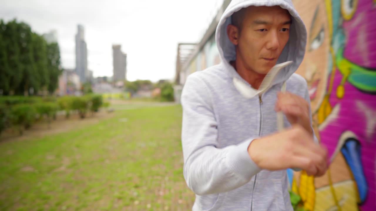 Chinese runner and boxer jogging and air boxing, workout in a city park in a fitness training session with graffiti street art wall and London city skyscrappers in the background