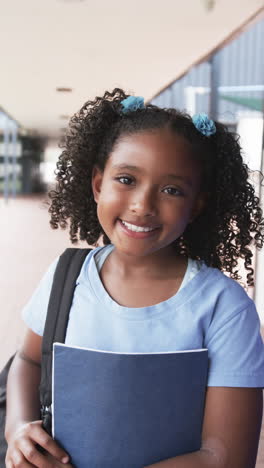 vertical video: in school, smiling girl holding notebook and backpack, ready for class