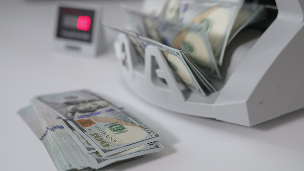 Lots of hundred dollar bills are calculated in the money machine. A wad of American dollars lies in front of equipment. Close up. Blurred backdrop.