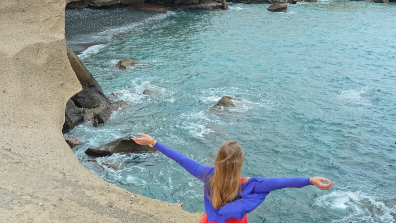 toma amplia de una mujer levantando los brazos frente a las olas del océano, día ventoso, inclinarse hacia arriba, día
