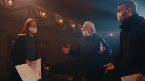 actors in face masks acting out quarrel on stage actress in mask screaming at adult actor near agitated senior man then throwing papers and walking away
