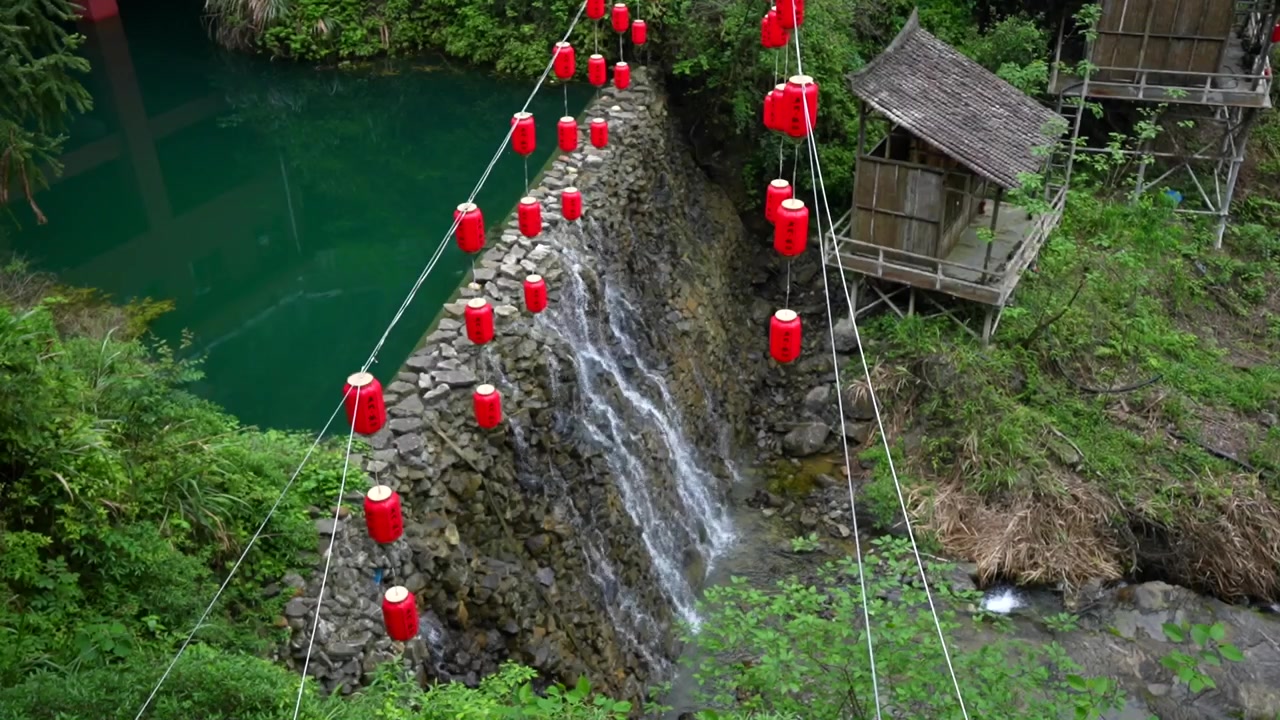 Çin'in Zhangjiajie bölgesinin yemyeşil manzarasında bir şelalenin üzerinde asılı kırmızı Çin fenerleri.