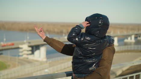 a father carries his son while pointing out something in the distance, engaging him in conversation,the child, dressed in a black jacket, rests his hand on his head, listening intently