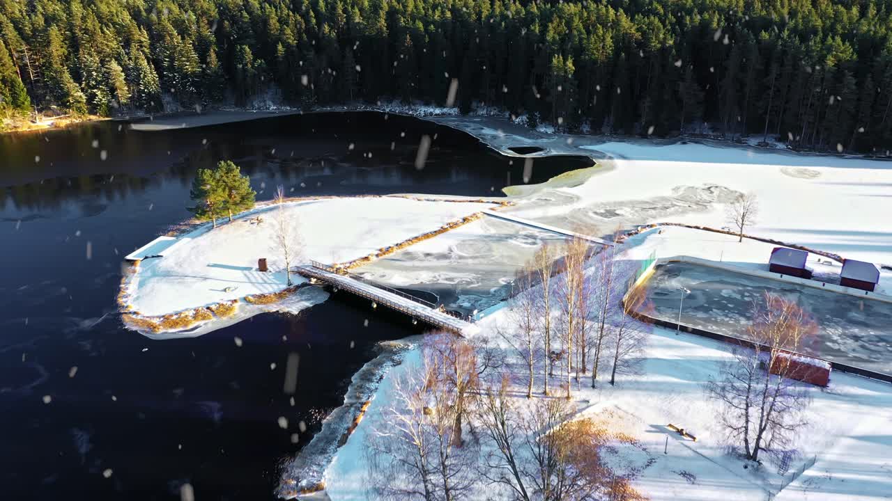 Lumipeitteinen saari ja järvenrantavyöhyke jäisen renkaan ympäröimänä aurinkoisena talvipäivänä, ilmakuva