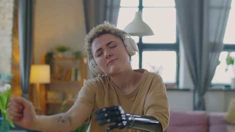 chica con brazo protésico en auriculares inalámbricos bailando en casa