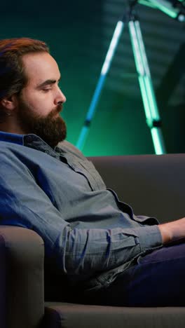 vertical video man working on laptop at home with tv show playing in background
