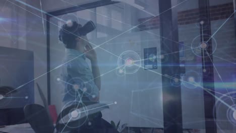 Animation-of-network-of-connections-over-caucasian-man-wearing-vr-headset-at-office