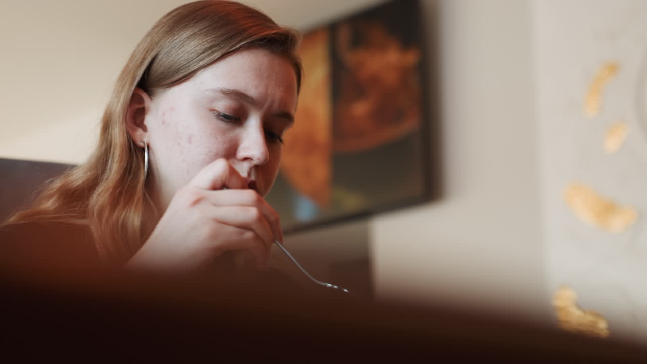 Jovem mulher pensativa provando salada em close-up, mastigação lenta e contemplativa, fundo suave com obra de arte emoldurada, bokeh suave, tons quentes, enquadramento íntimo à mão, sutil ritual de nutrição.