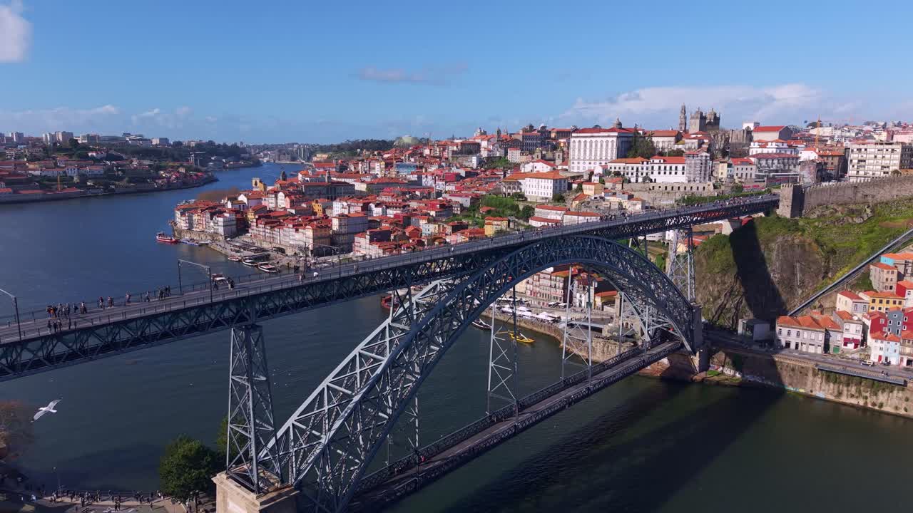 Drone shot of Luiz I bridge over river Douro with pedestrians and metro rail line at upper deck and public transportation road at lower deck, connecting Porto and Vila Nova de Gaia