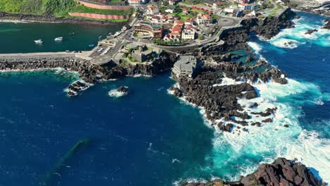 panoramic aerial pullback reveals porto moniz natural pools of vibrant blue ocean water and terraced city, madeira portugal